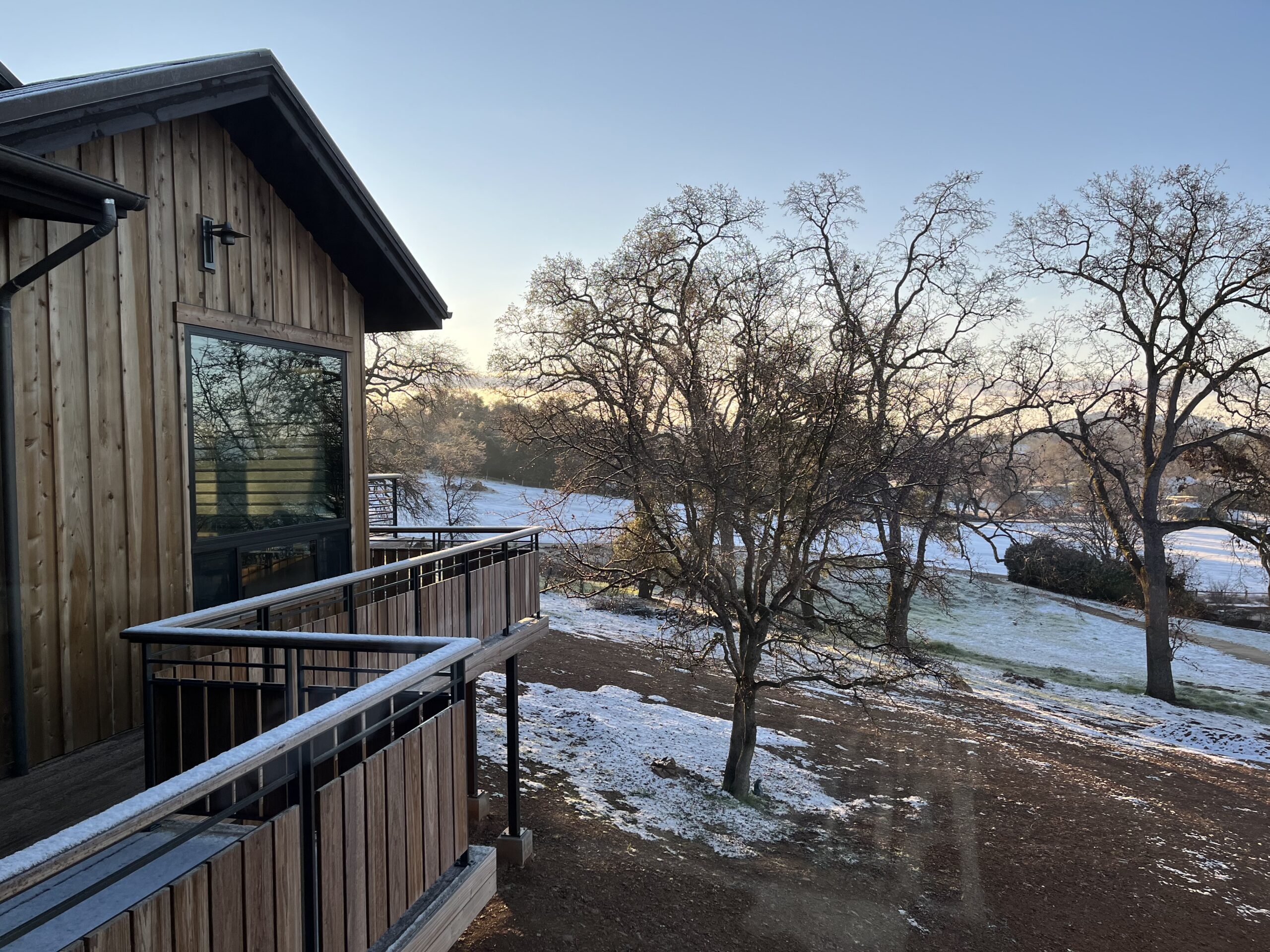 IMG_3820 Wooden building with a balcony overlooking a frosty landscape with sparse snow and leafless trees under a clear sky.